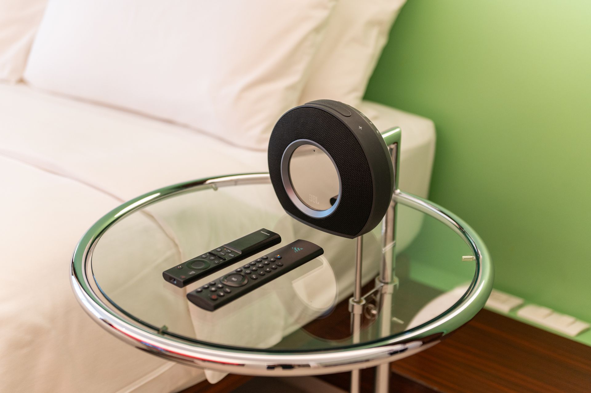 Two remote controls sit on a glass table next to a bed