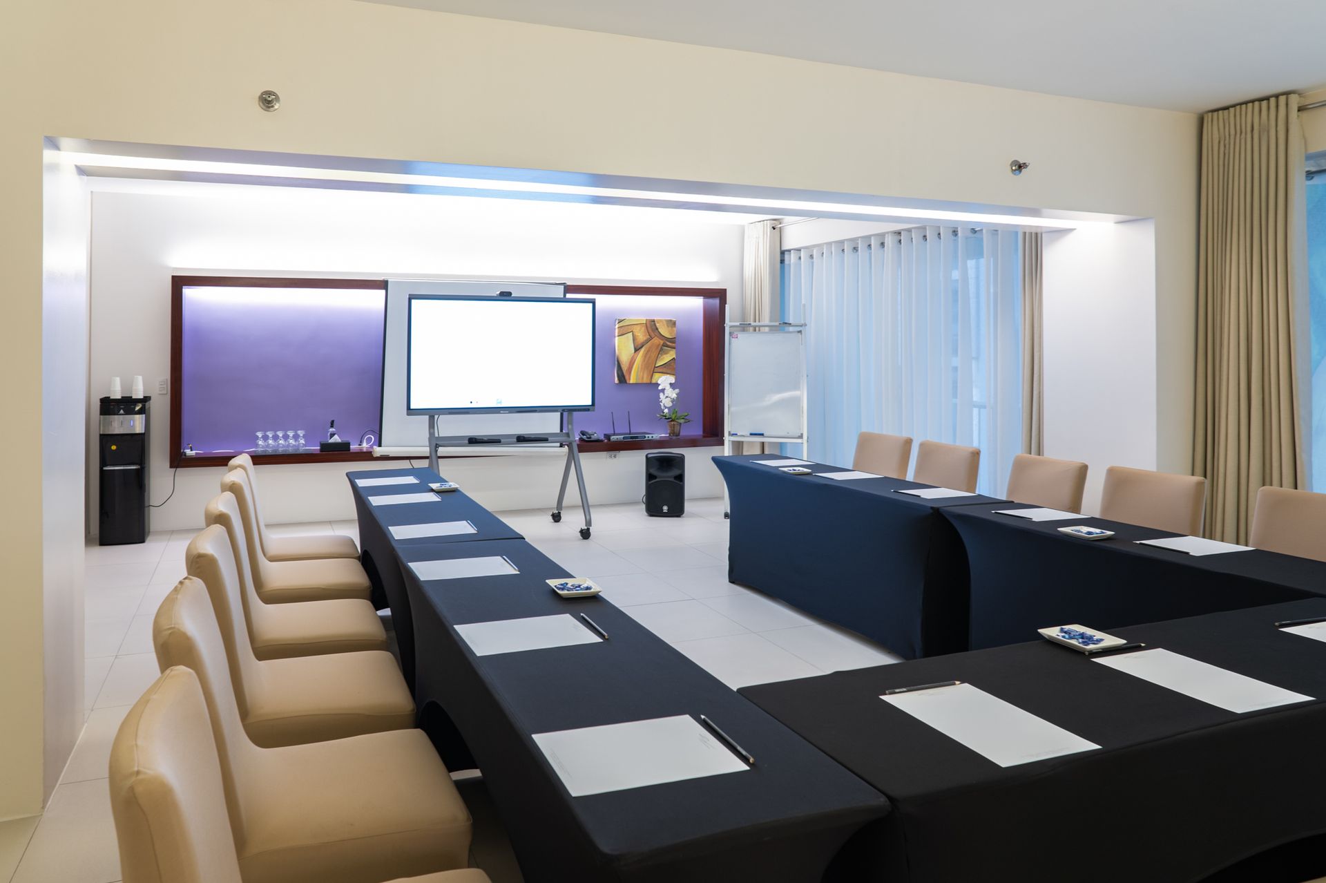 Conference room with U-shaped table setup, projector screen, and chairs.