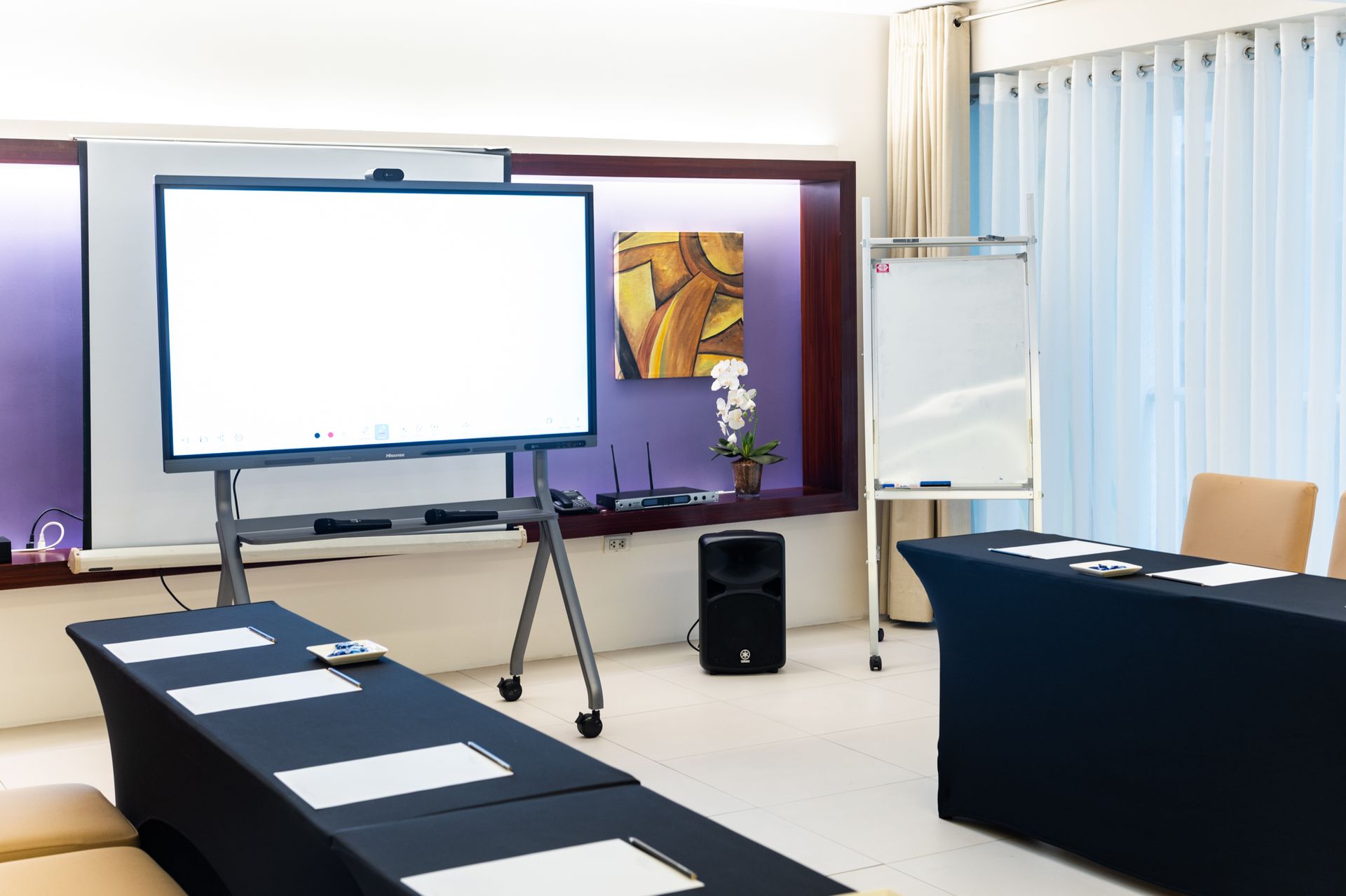 Conference room with a large screen, whiteboard, and tables set up for a presentation.
