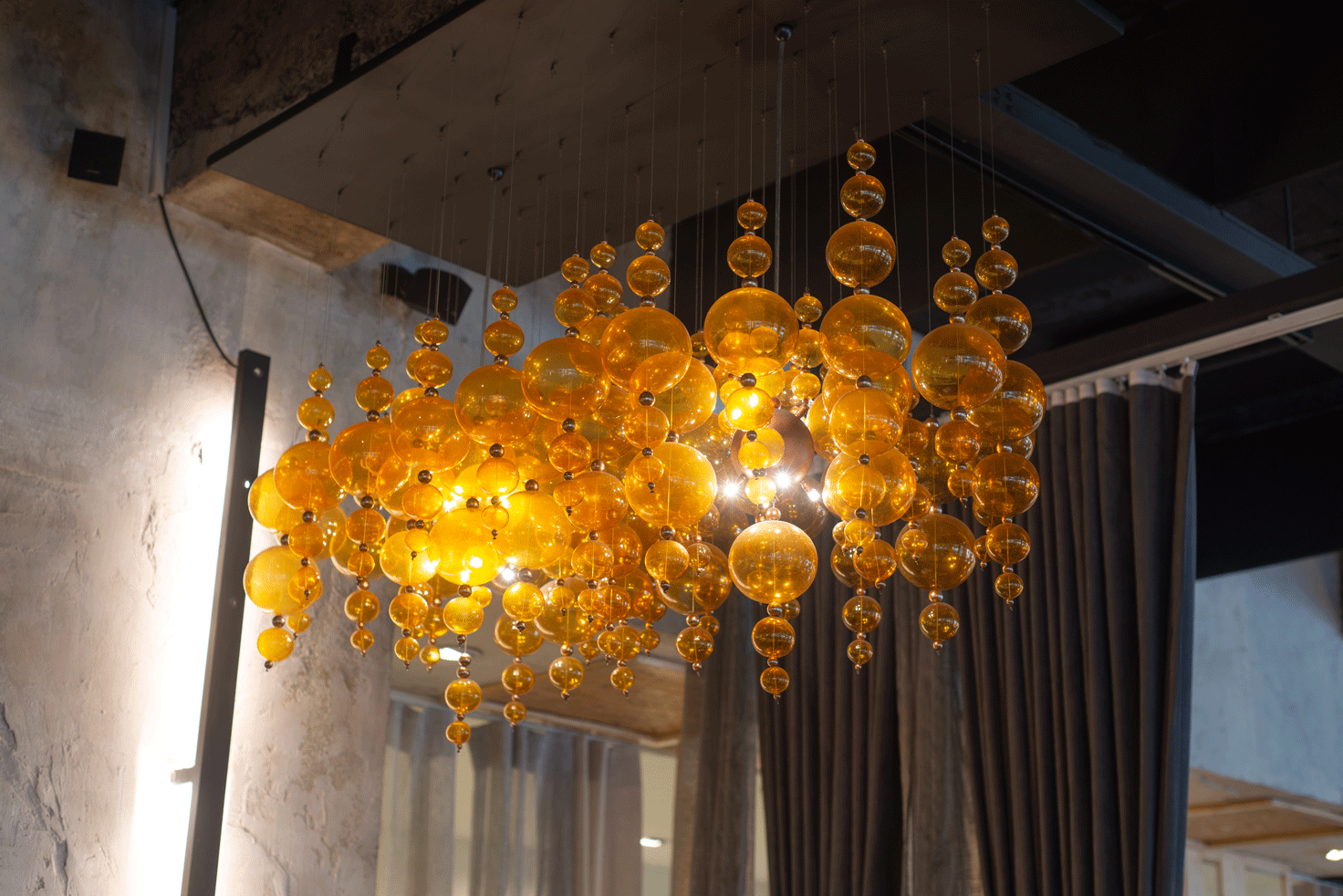 Golden orb chandelier hanging from a concrete ceiling, illuminating a dim room.