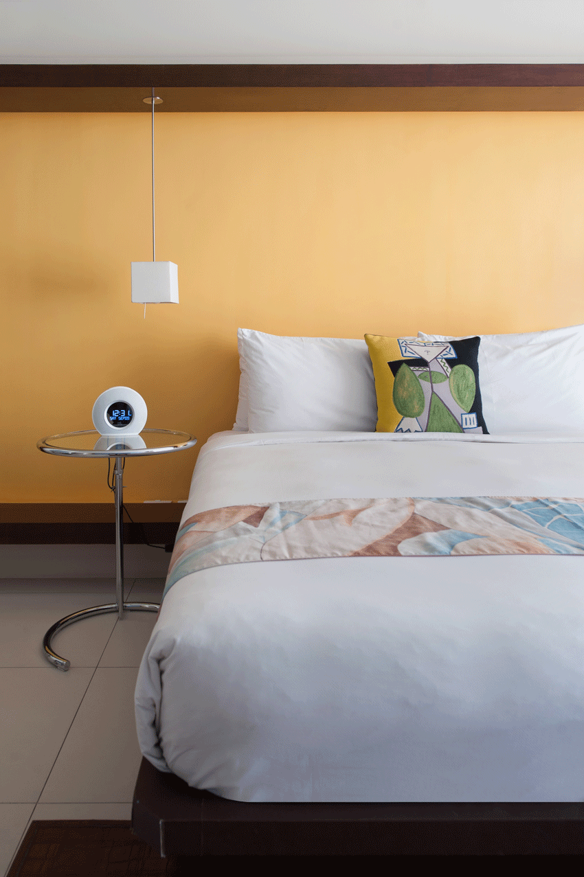 A bed with white sheets and pillows in a hotel room with a yellow wall.