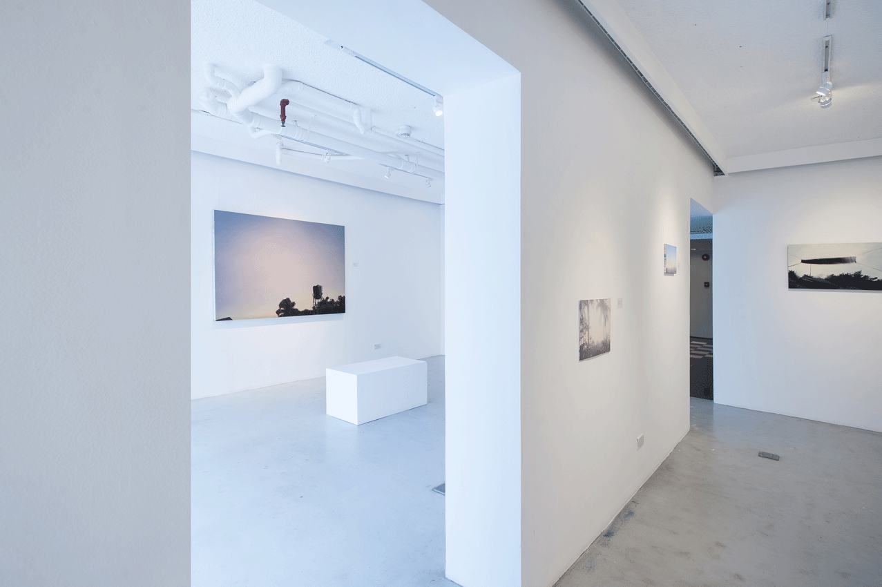 Modern art gallery interior with white walls, paintings, and a white bench.