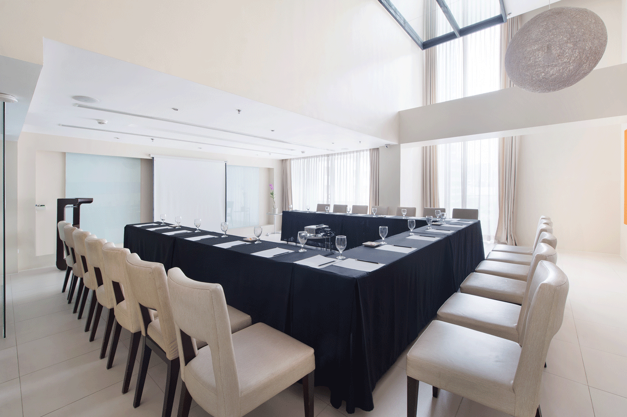 A modern meeting room with a U-shaped table covered in black cloth. White chairs are arranged around the table.