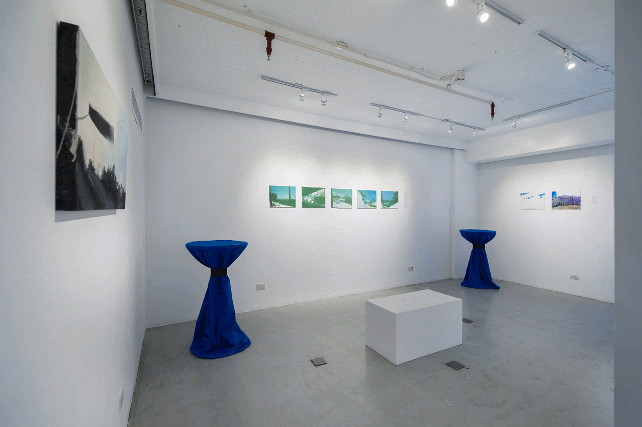Art gallery interior with white walls, paintings, two blue cocktail tables, and a white cube.