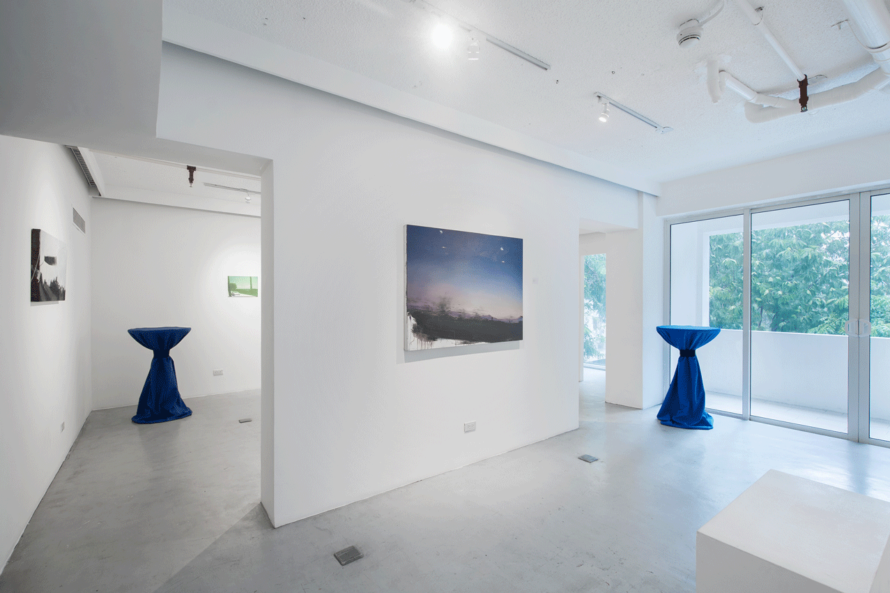 An art gallery interior with white walls, paintings, and blue cocktail tables.