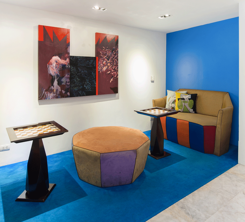 Room with art, seating, and a blue carpet. Beige couch with patchwork detail, colorful pillows. Modern decor.