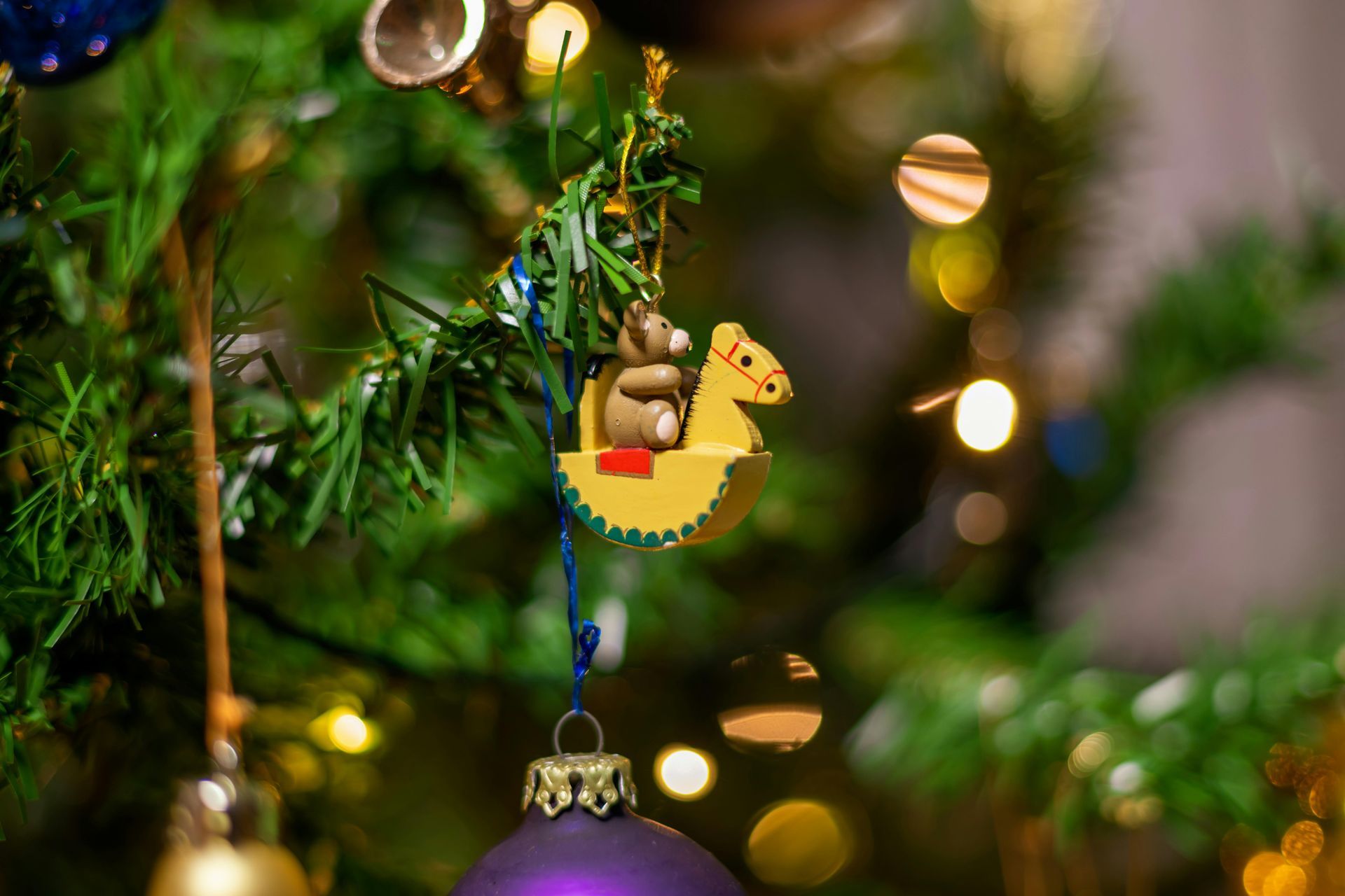 Christmas tree ornament: wooden rocking horse with small bear, on tree with purple and gold ornaments.