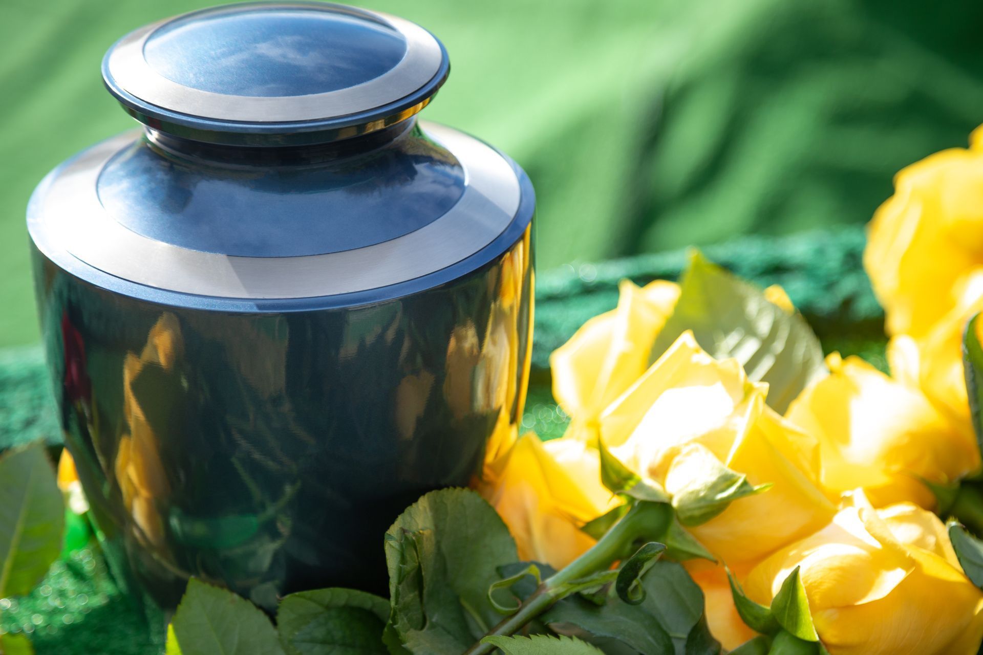 a black urn sitting next to yellow roses on a green table .