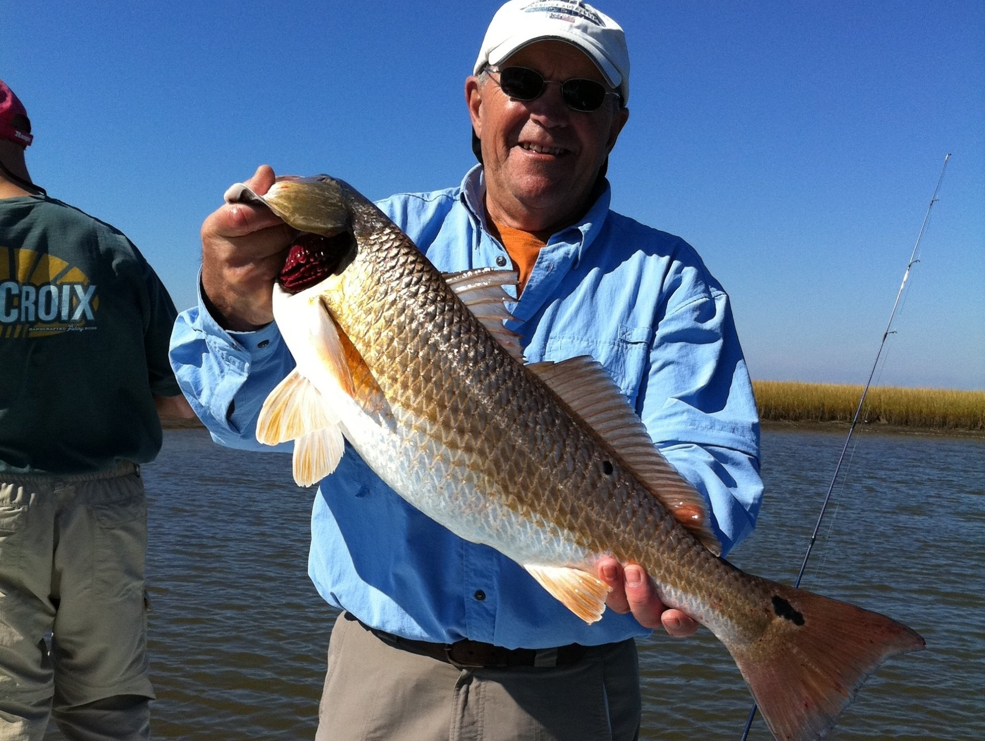 A man in a croix shirt holds a large fish