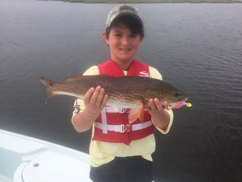 A young boy wearing a life vest is holding a large fish