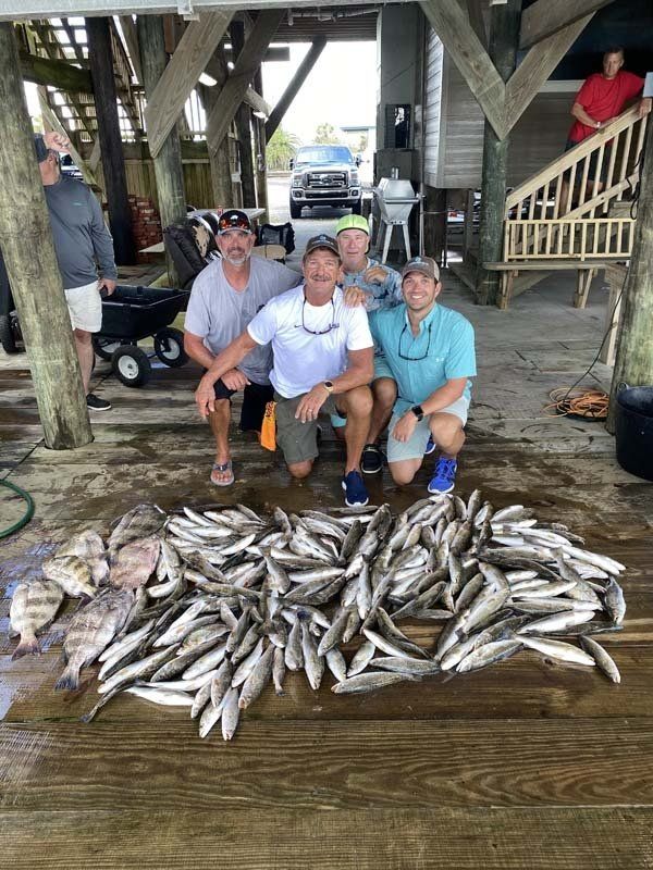 A group of men are posing for a picture with a pile of fish.