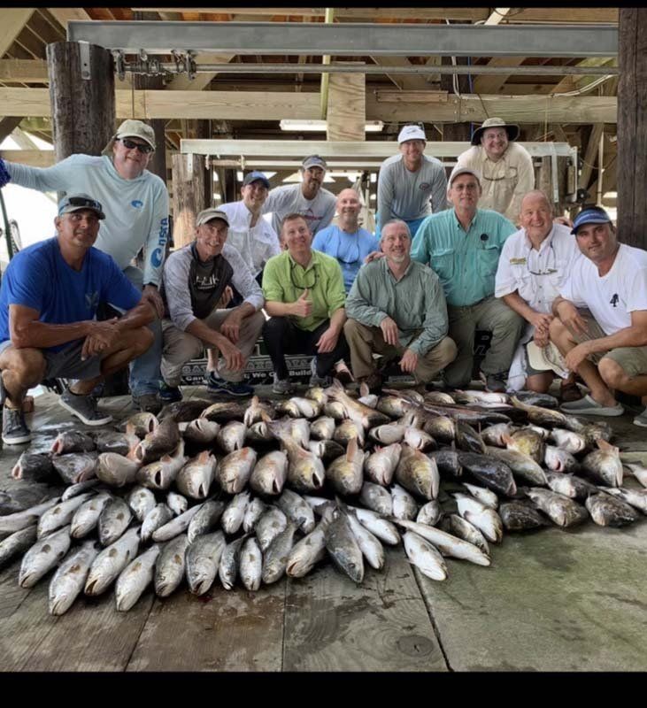 A group of men are posing for a picture in front of a pile of fish