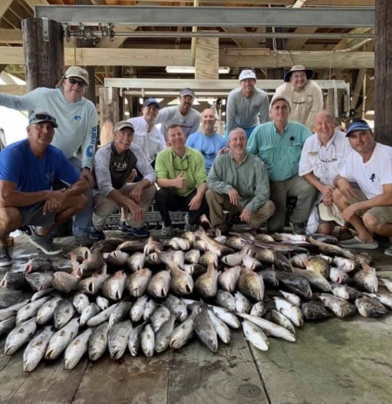 A group of men are posing for a picture in front of a pile of fish