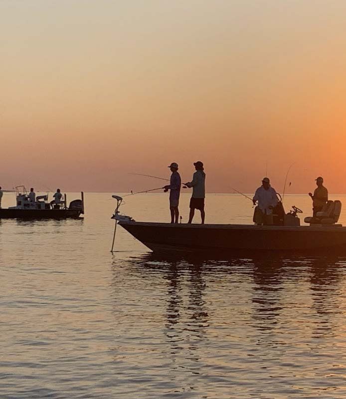 A group of people are fishing from a boat in the ocean at sunset.