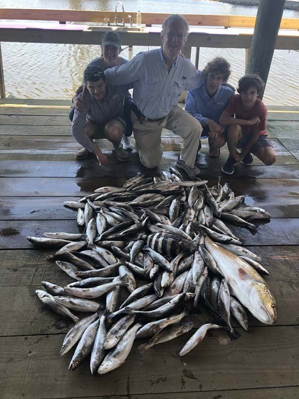 A group of people are posing for a picture with a pile of fish.