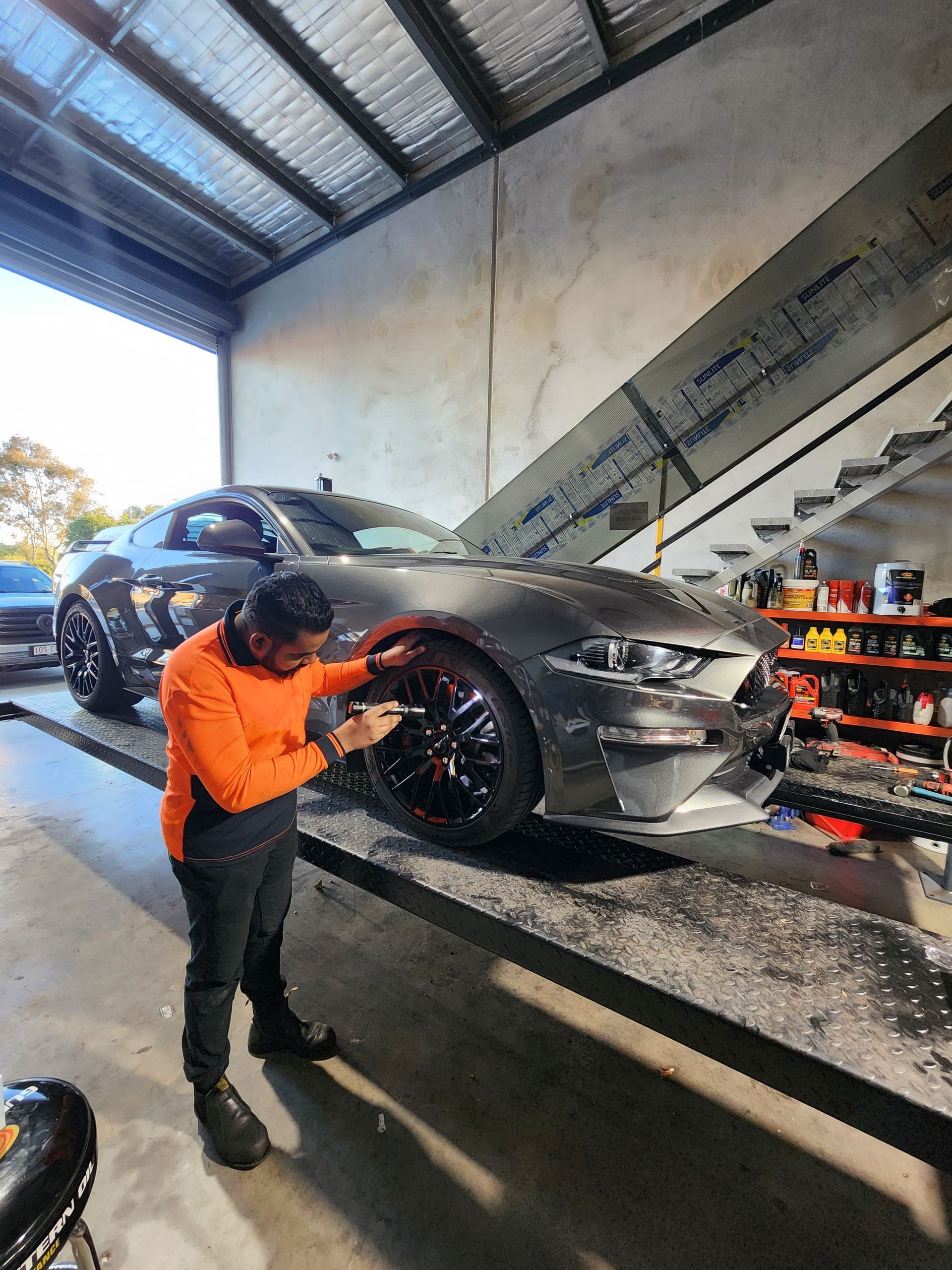 Man Working on a Gray Ford Mustang in a Garage. He is Wearing Orange Workwear — QA Oxley in Oxley, QLD