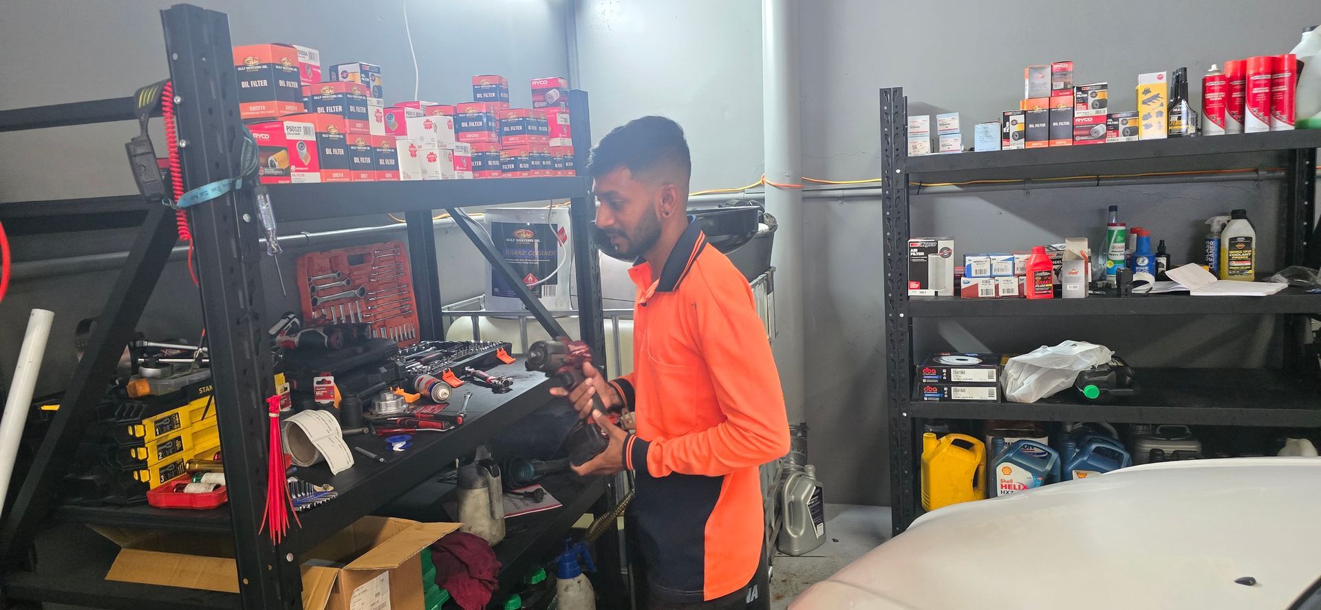 A Man in an Orange Shirt Stands Inside a Garage With Shelves of Various Items — QA Oxley in Sinnamon Park, QLD