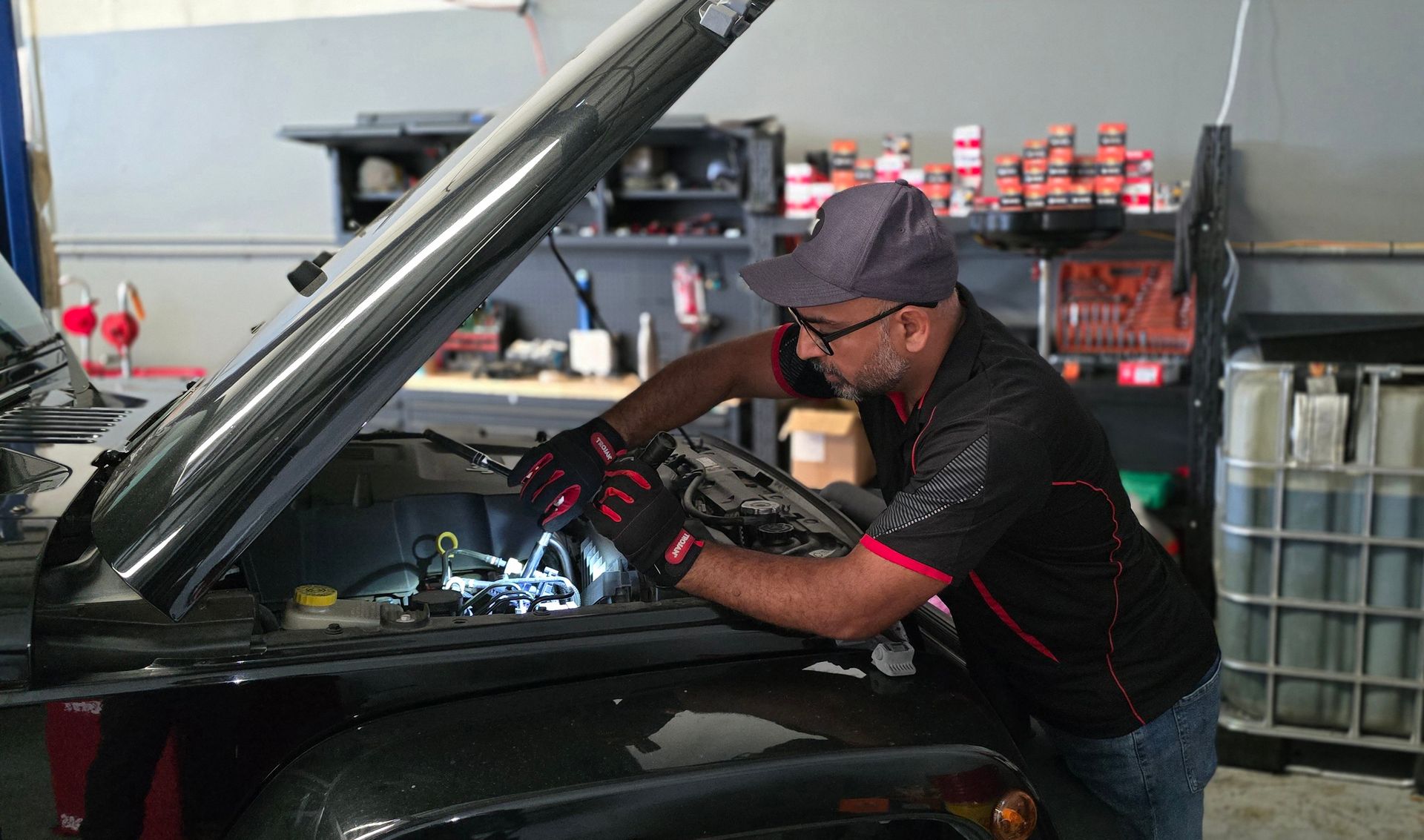 Mechanic Working on a Car Engine in a Garage. He Wears Gloves and a Hat, With the Hood Open — QA Oxley in Oxley, QLD