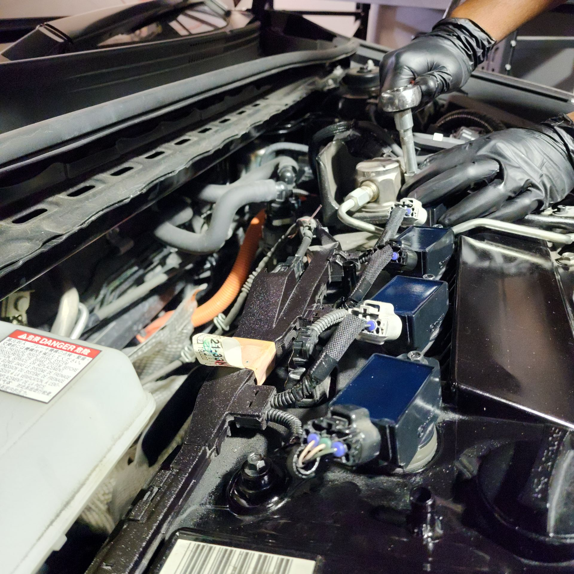 Hands in black gloves working on car engine, using a wrench.