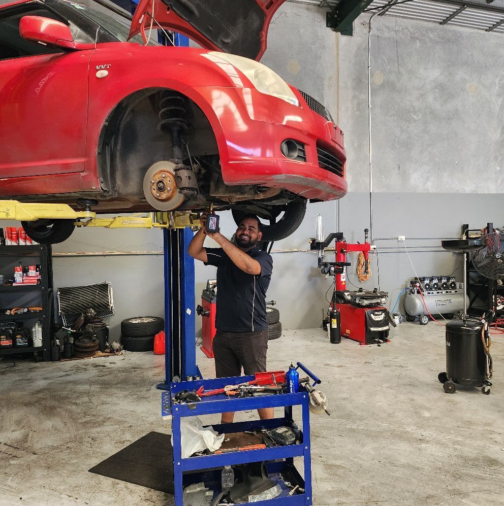 Mechanic Working on a Red Car Lifted on a Hoist in a Repair Shop — QA Oxley in Oxley, QLD