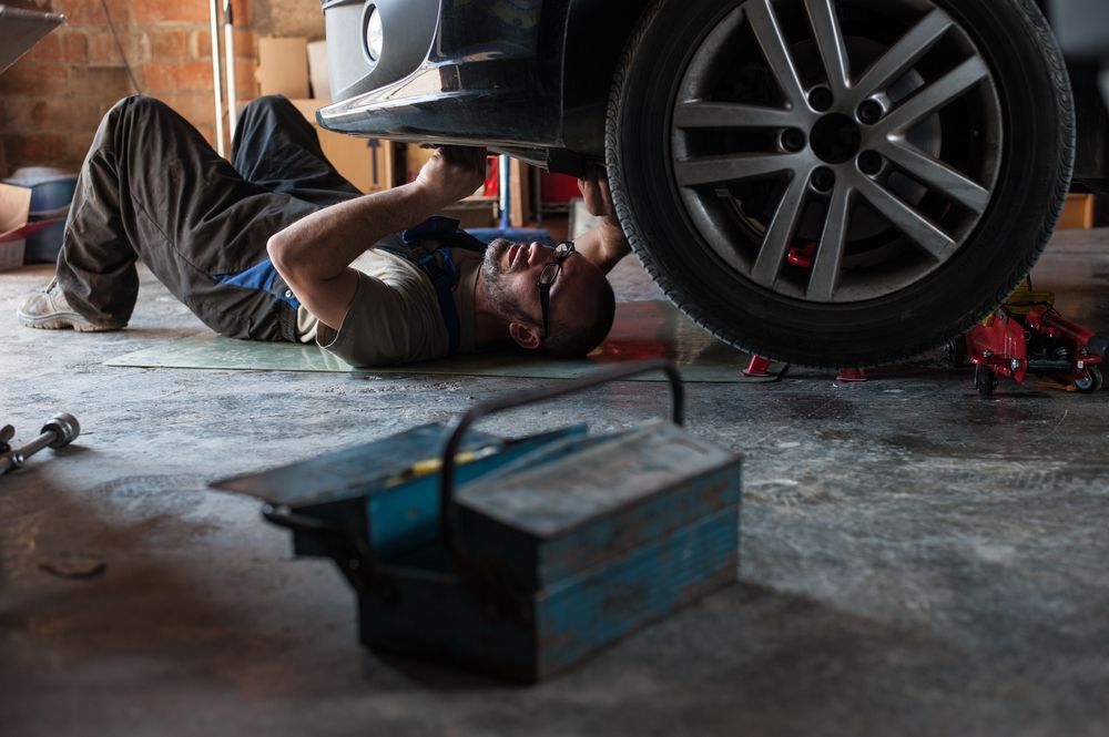 Mechanic Lying Under a Car in a Garage, Working on It; Toolbox in Foreground — QA Oxley in Oxley, QLD