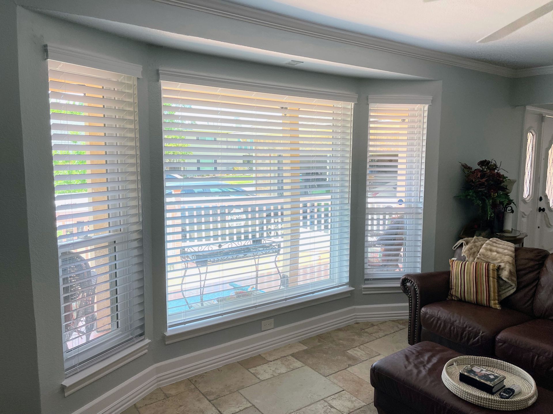 Bay window with white blinds, blue walls, and a brown leather couch.