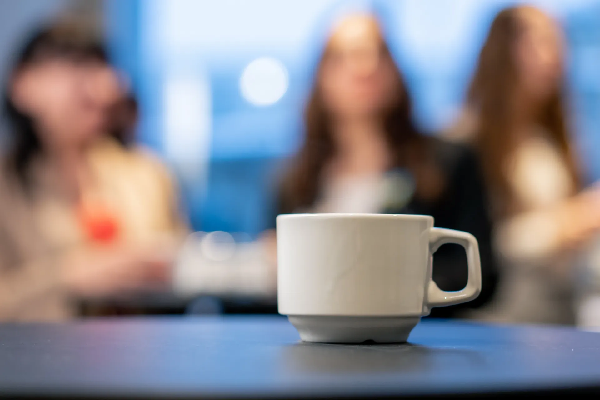 En kopp kaffe står på et bord foran en gruppe mennesker.