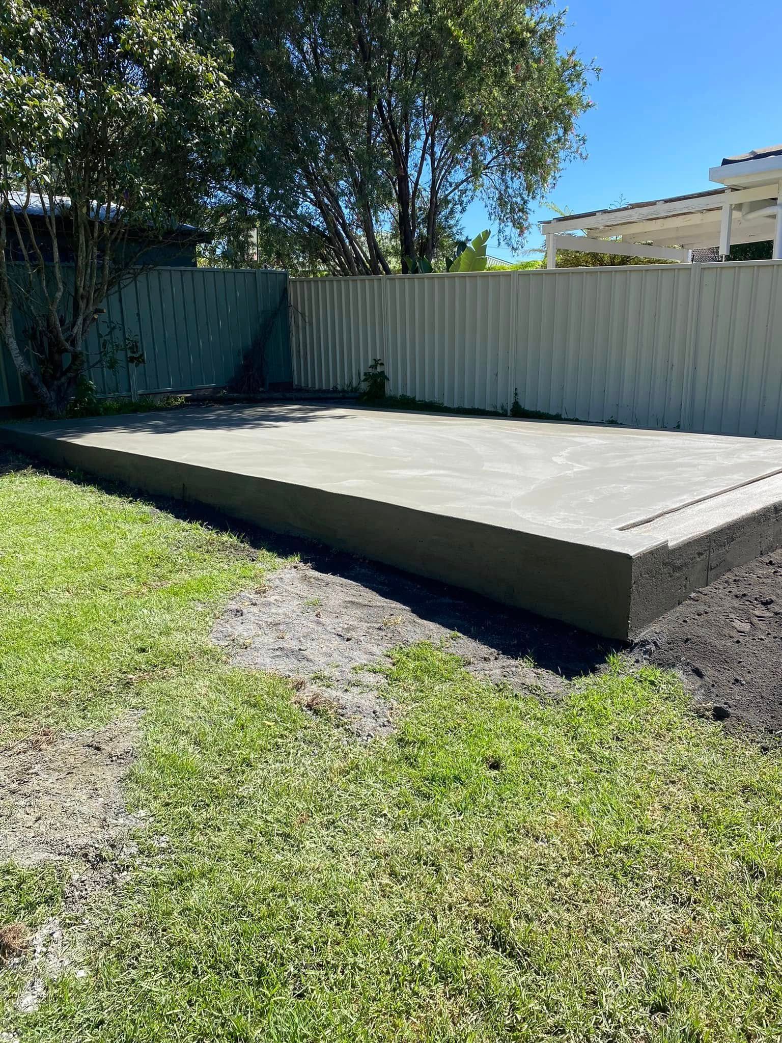 Concrete Slab In A Grassy Backyard Beside A Metal Fence — BJ's Concreting in North Nowra, NSW