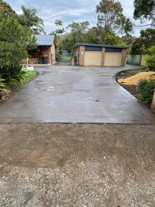 Wet concrete driveway leading to a double garage, surrounded by trees and shrubs — BJ's Concreting in Callala Bay, NSW
