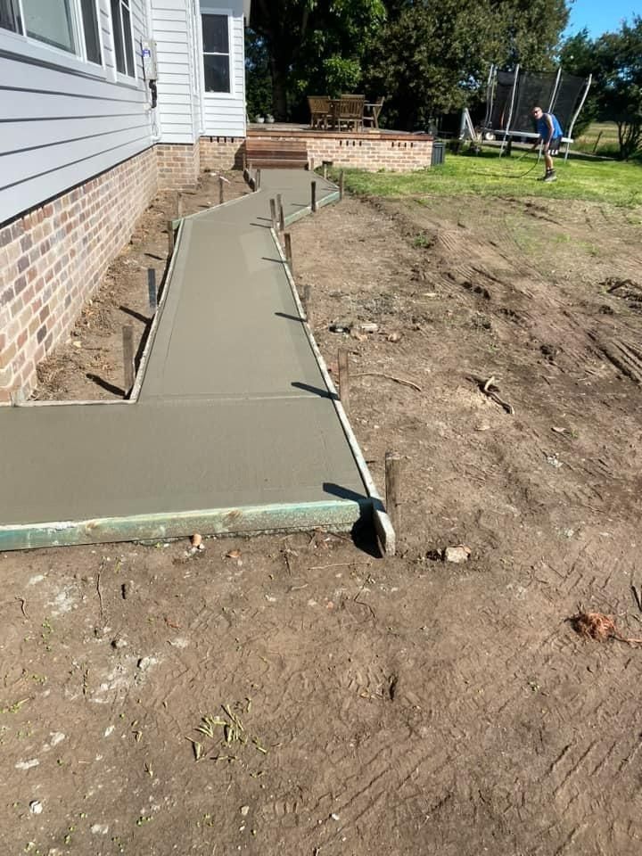 Fresh concrete walkway forms beside a house, with a brick foundation and dirt yard around it. — BJ's Concreting in Huskisson, NSW