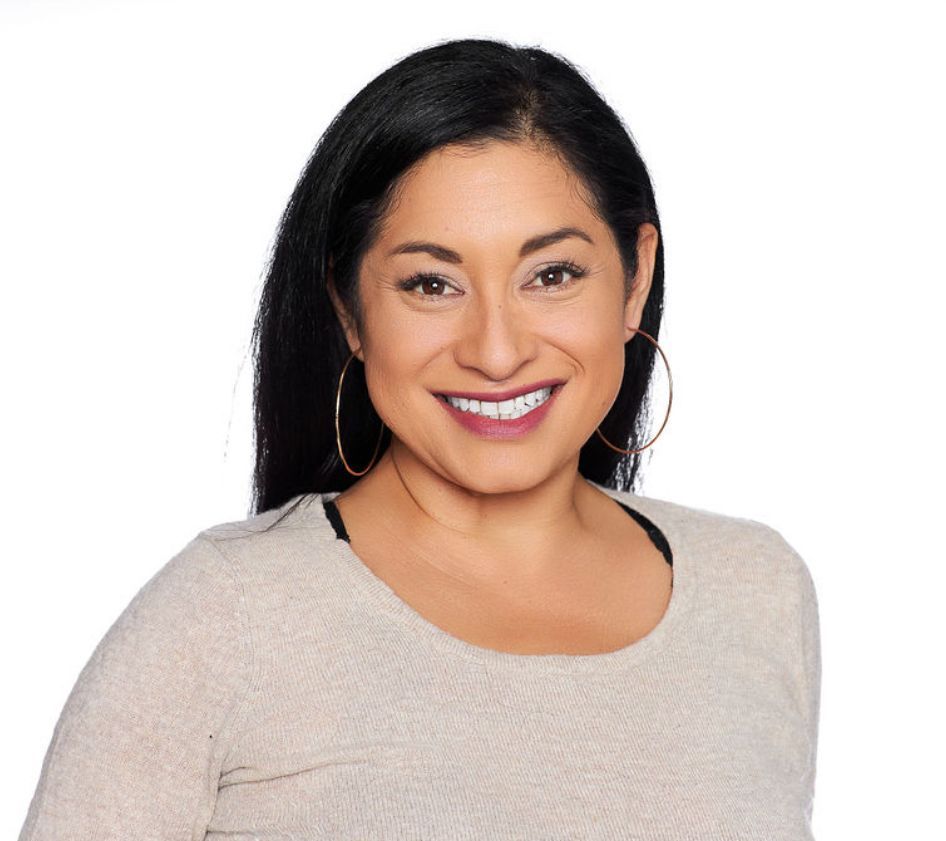 A woman wearing a tan sweater and hoop earrings is smiling for the camera.