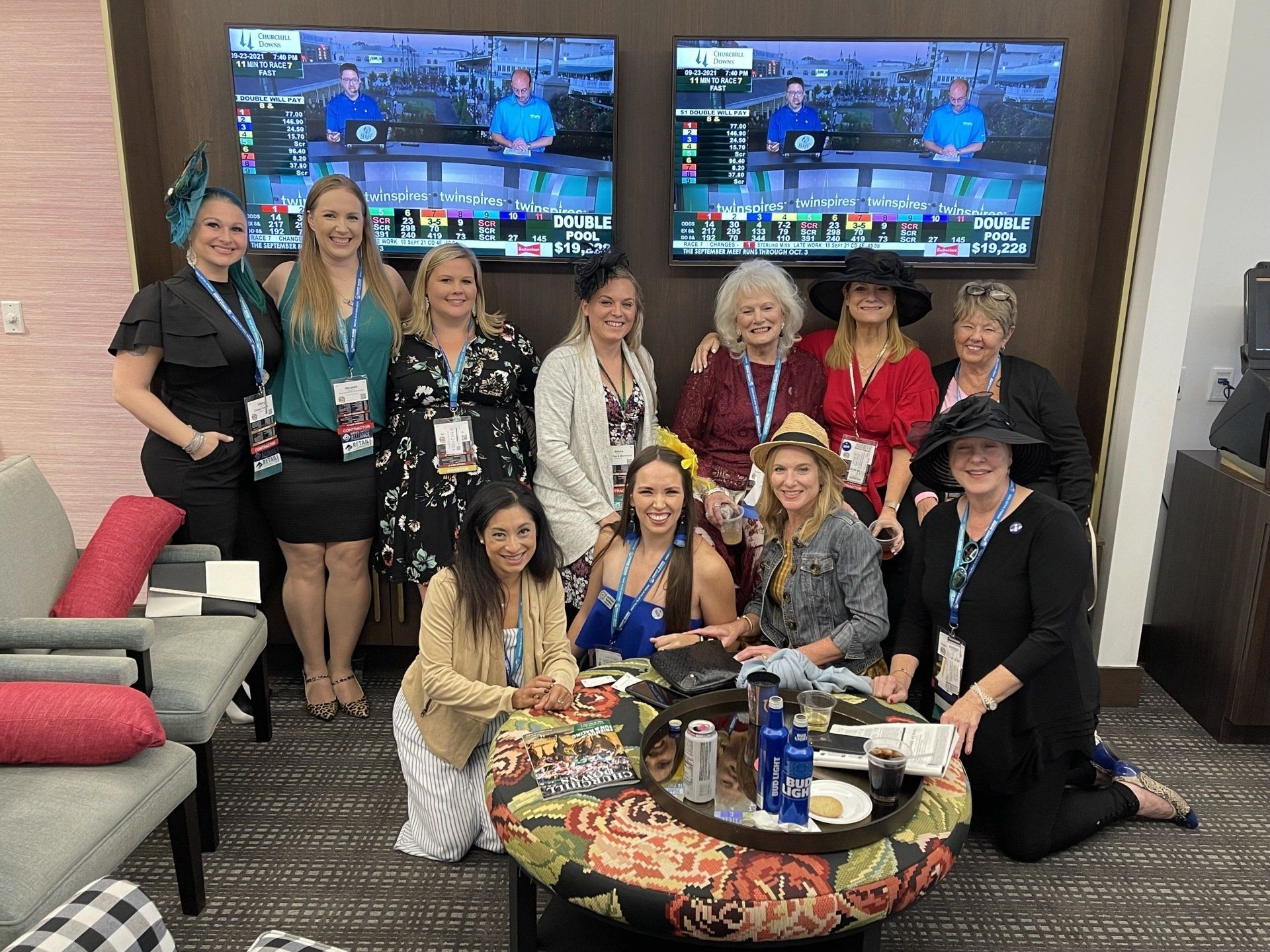 A group of women are posing for a picture in front of two televisions.