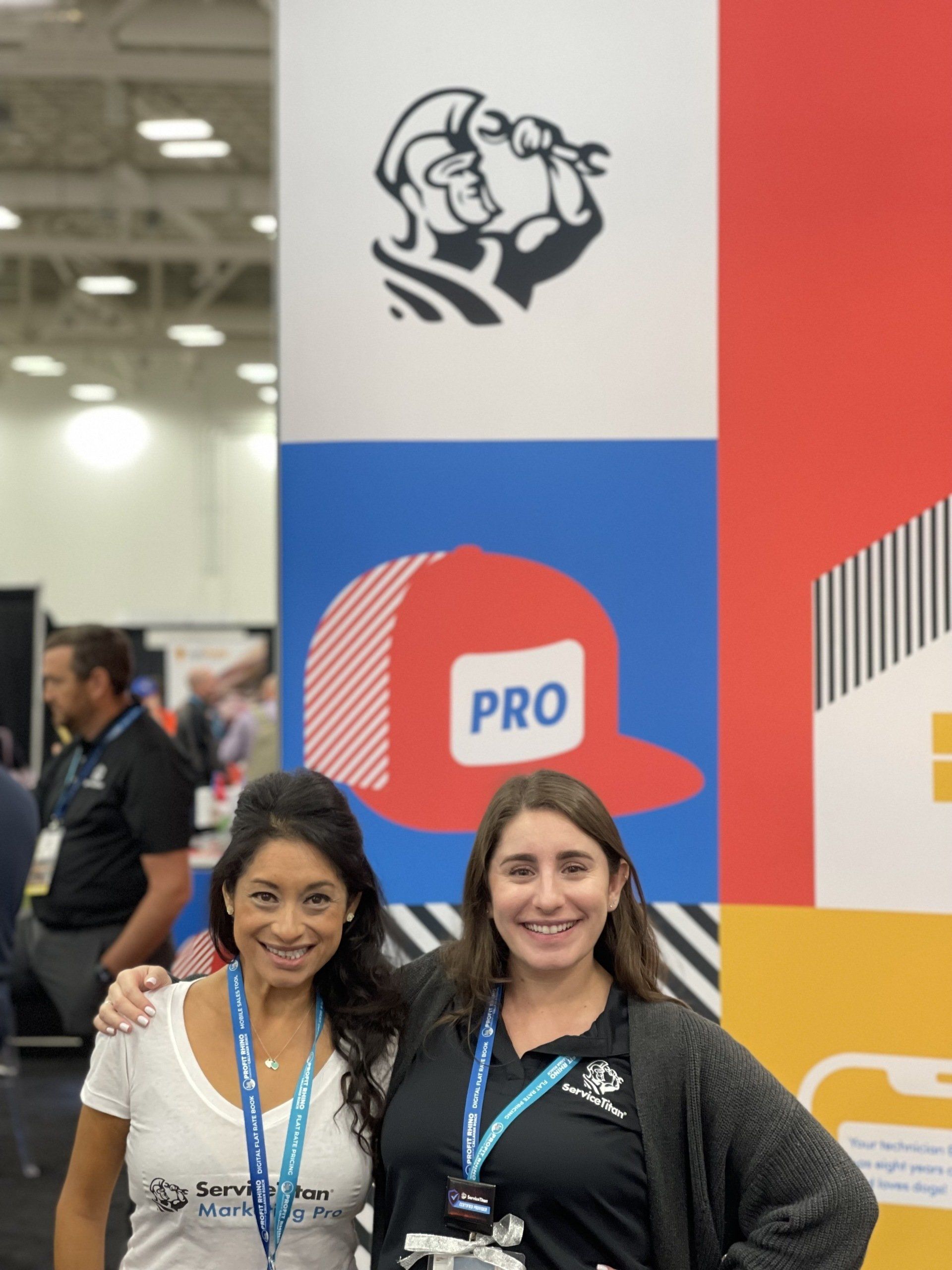 Two women are posing for a picture in front of a sign that says pro