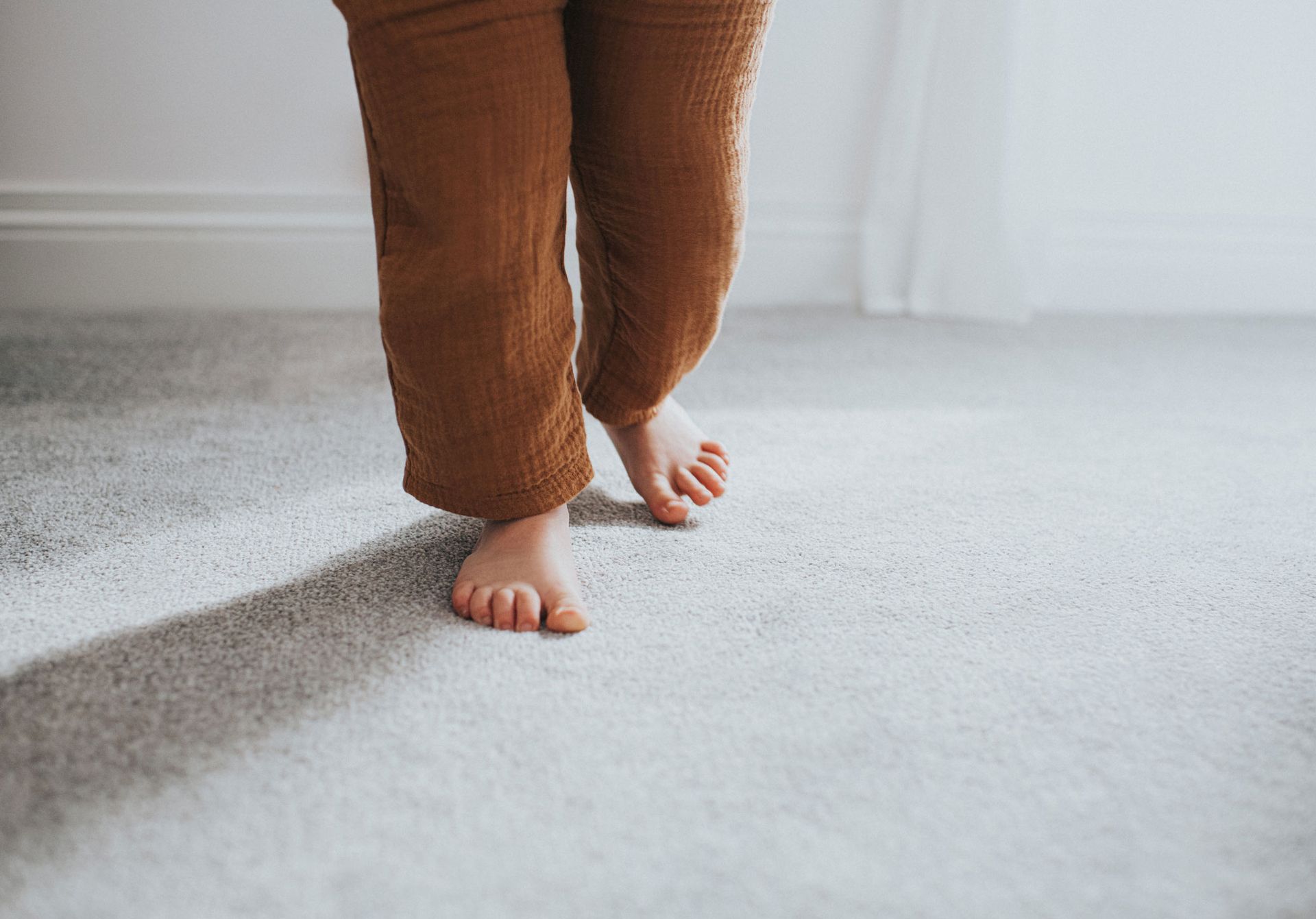A baby is walking barefoot on a carpet.