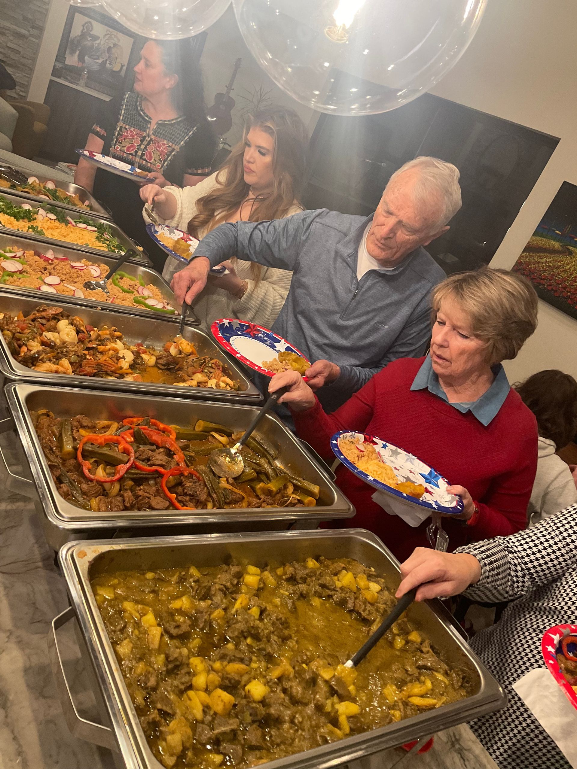 A group of people are standing around a buffet table eating food.