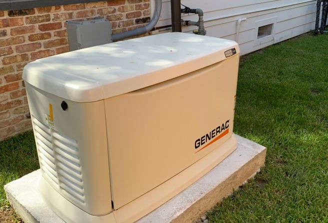 A generator is sitting on top of a concrete base in front of a brick house.