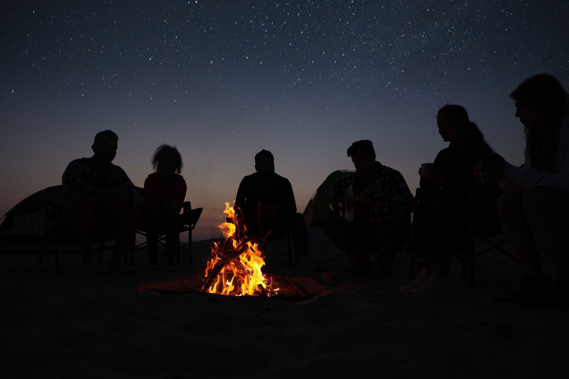 Bonfire Night in Reading - A group of people are silhouetted against a campfire at night with a starlit sky overhead. Two tents can be seen in the background.