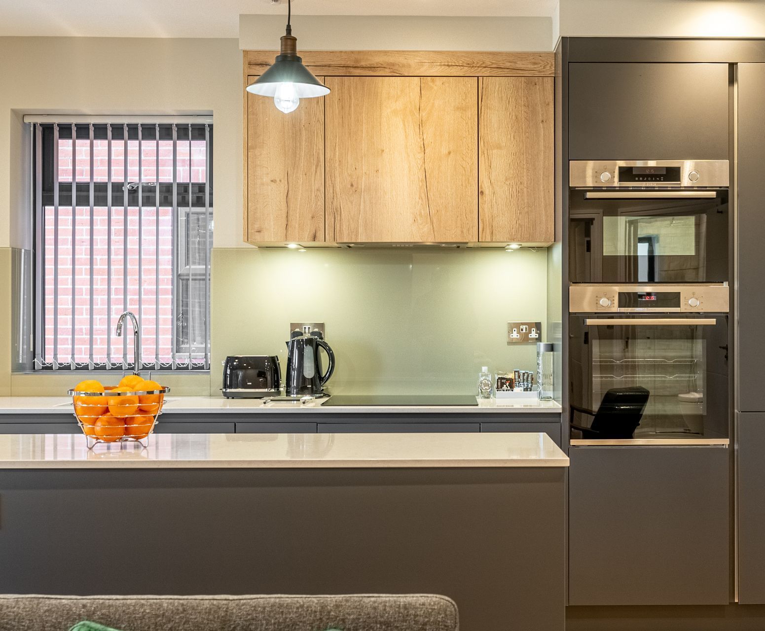 Modern kitchen with built-in ovens, a countertop with appliances, and a bowl of oranges.