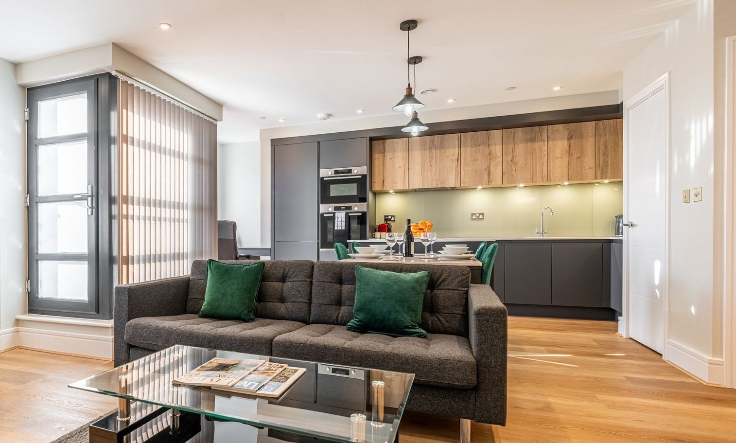 Modern living room with dark gray sofa, open kitchen, and large window.