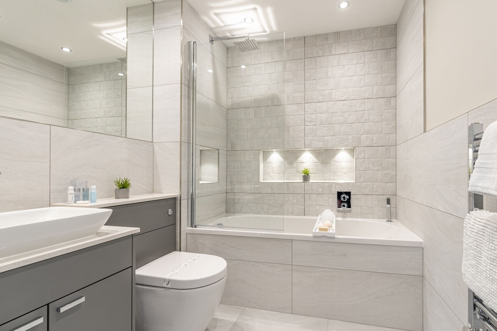 Modern bathroom with a bathtub, wall-mounted toilet, sink, and built-in shelf lighting.