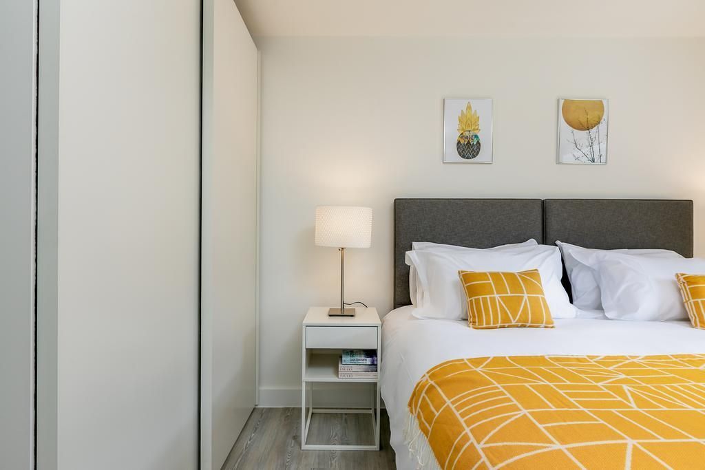 Modern bedroom with a gray headboard, yellow accents, white bedding, and a bedside lamp.