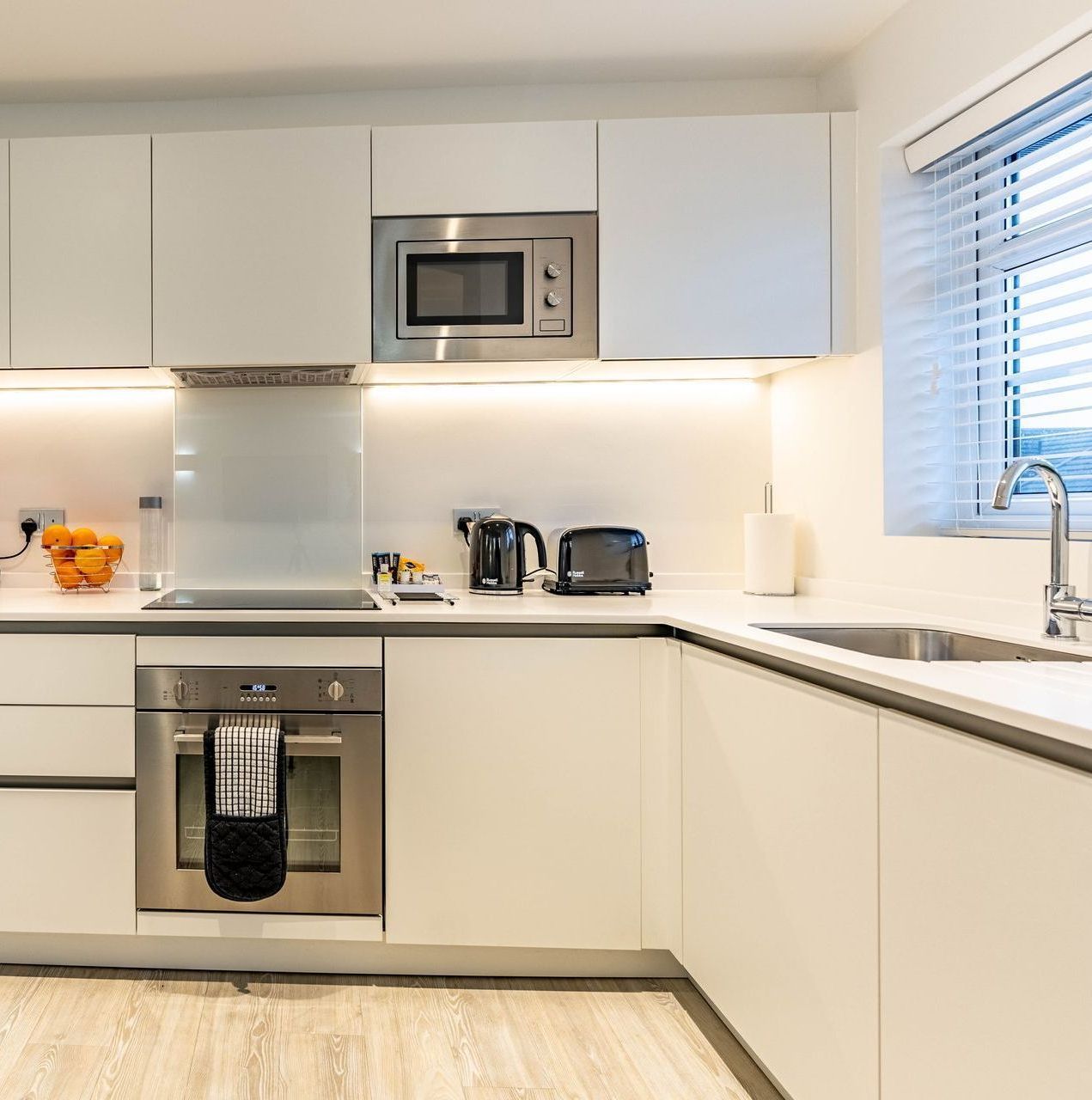 Modern kitchen with white cabinets, built-in appliances, countertop appliances, and a window.
