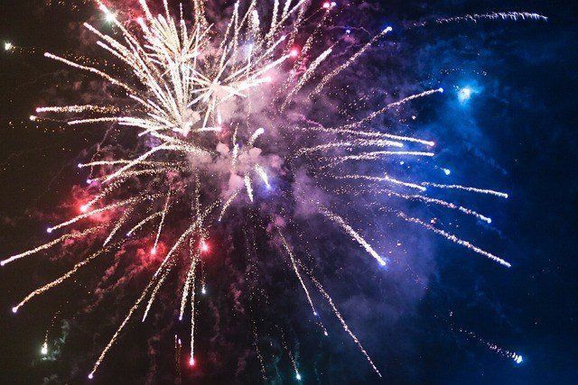 Colorful fireworks explode in the night sky, creating bright bursts of light with shades of red, blue, and white.