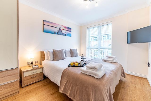 A neatly made double bed with folded towels, a breakfast tray, and a large window in a bright bedroom.
