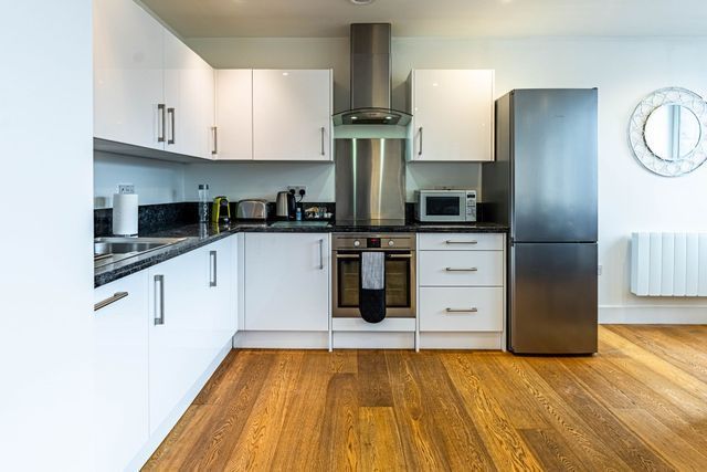 Modern kitchen with white cabinets, built-in appliances, countertop appliances, and a window.