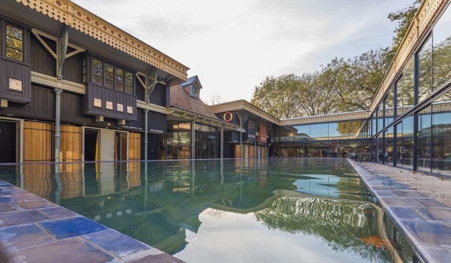 Reflective pool in front of a dark wooden building with glass windows, under a blue sky.
