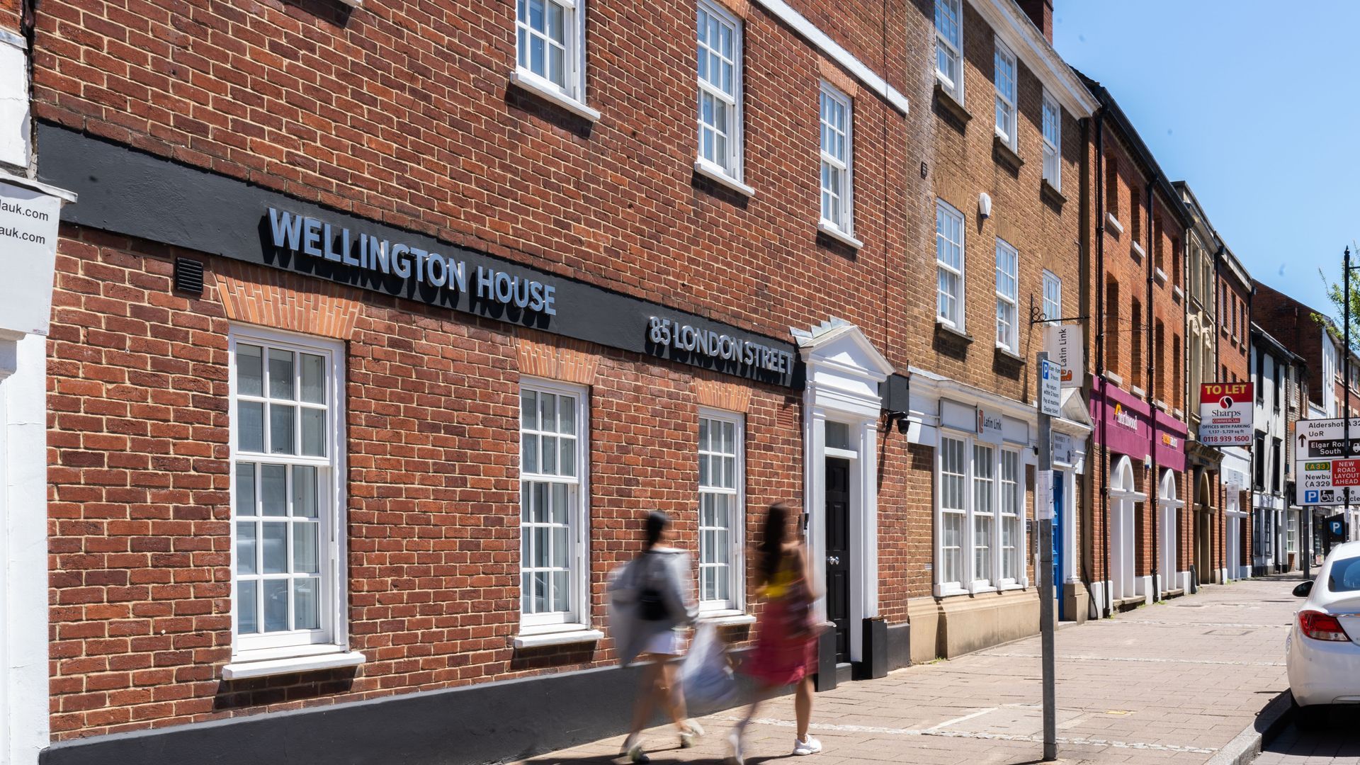 Two people walk past a brick building with signs reading 