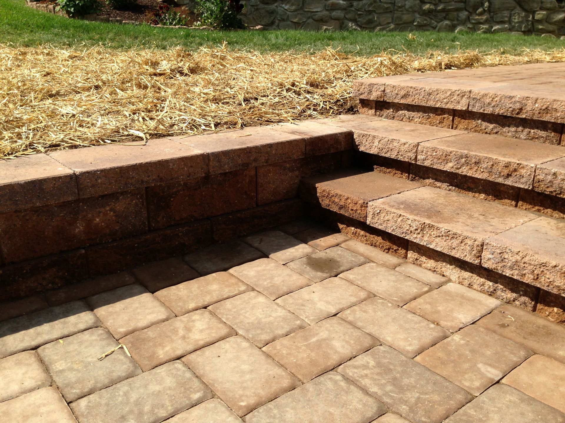 Brick patio with steps leading up to a raised garden bed and grass.