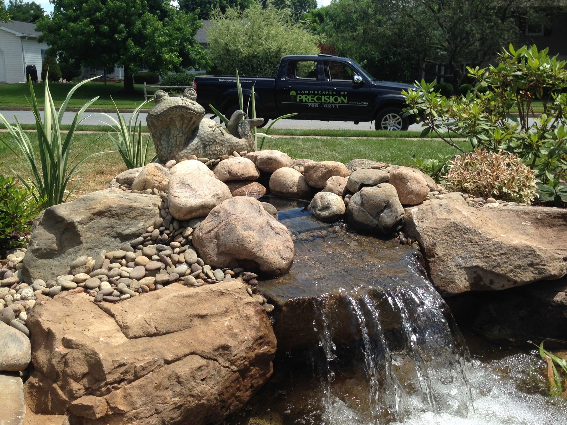 Water feature with waterfall cascading over rocks, small plants, and a truck in the background.