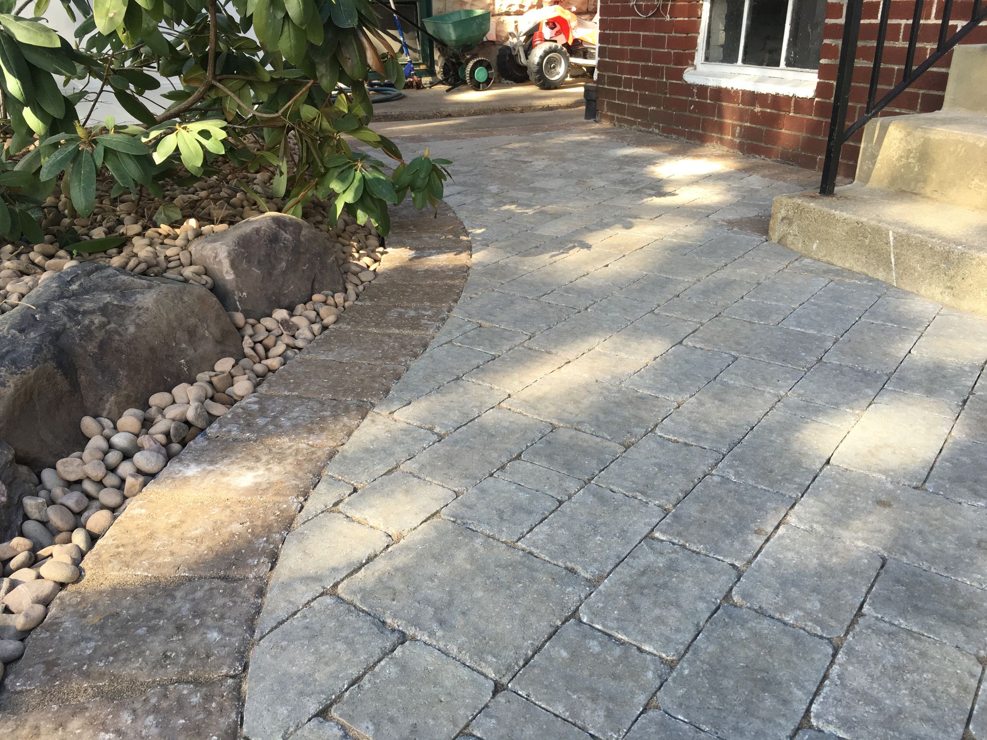 Brick walkway curving by large rocks and brick building, sunny Mechanicsburg, PA.